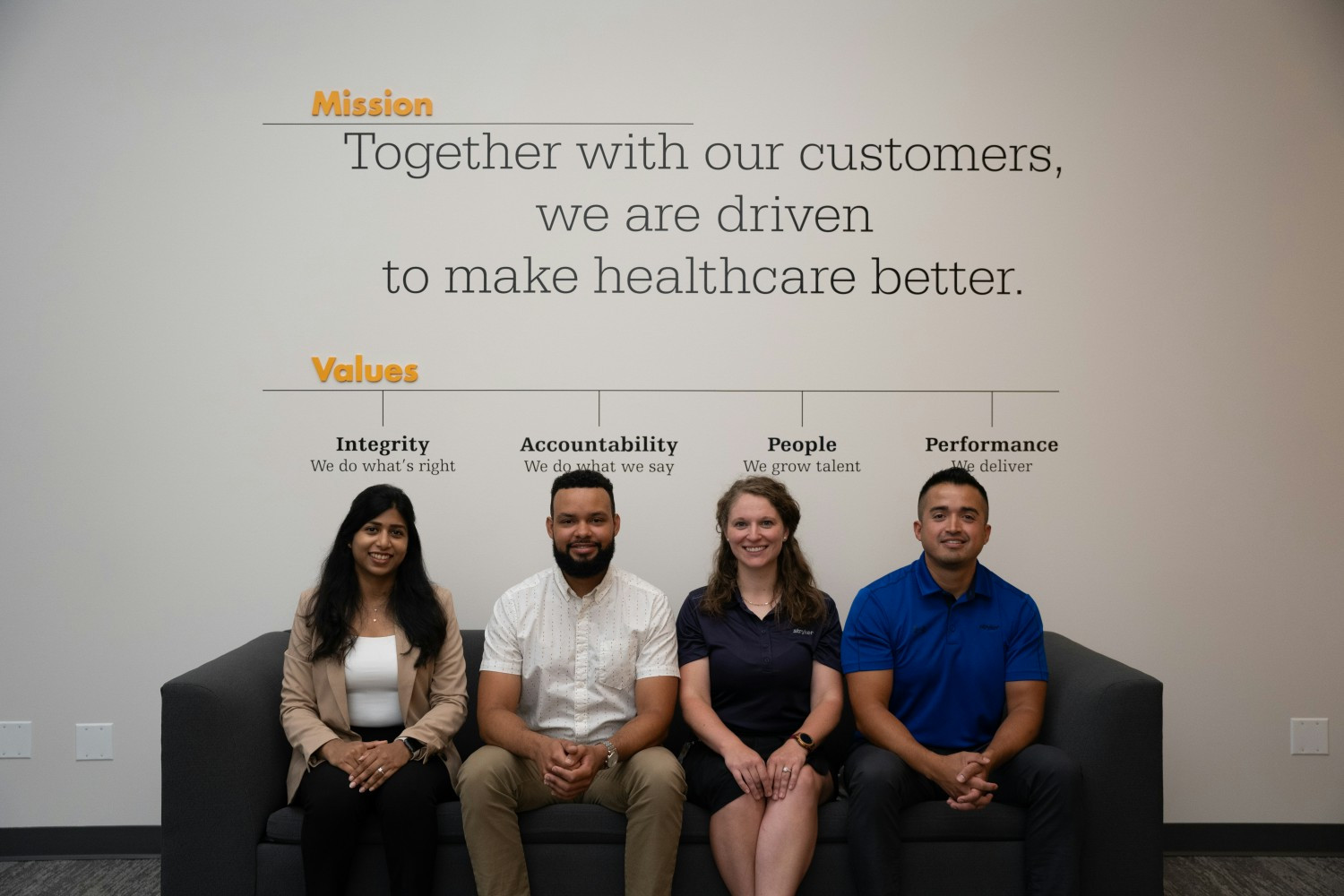  Stryker employees sit in front of wall painted with the company's values statements.