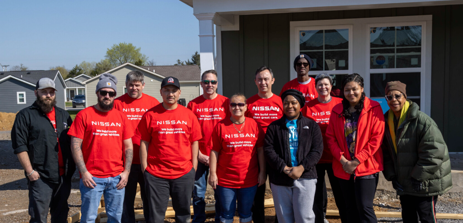 Nissan team volunteers stand up and smiling, uniting for community service.