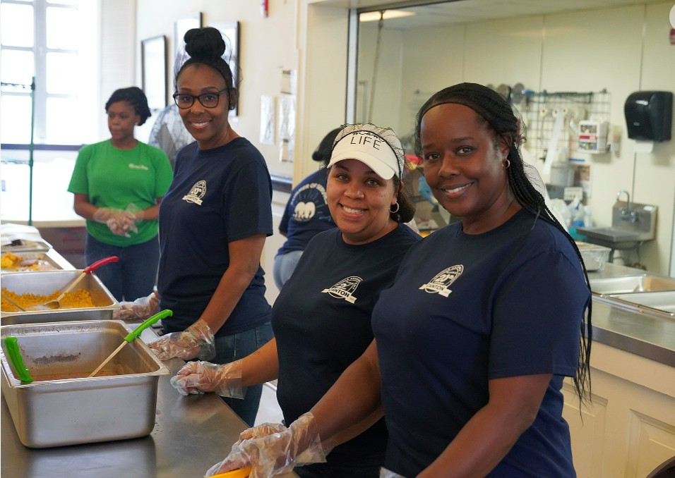 Nissan female volunteers in blue shirt serving food in a community kitchen setting.