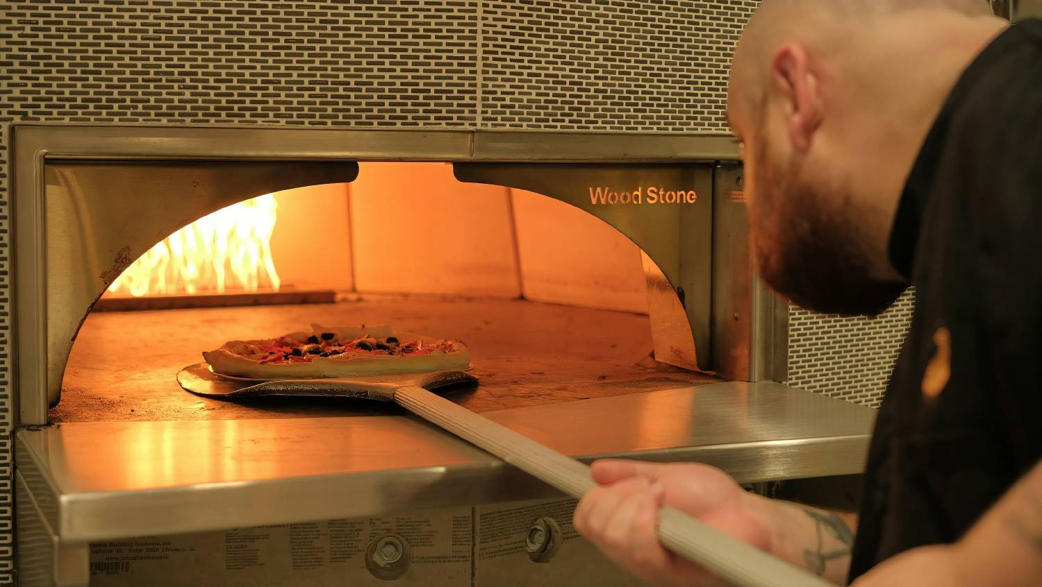 chef taking pizza out of pizza oven
