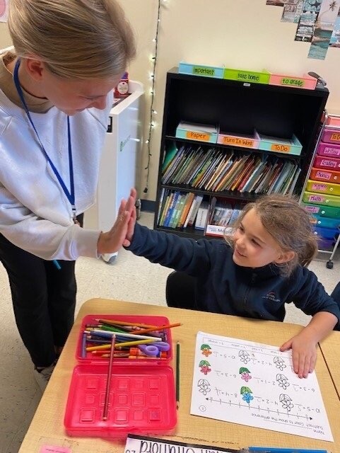 A teacher at Mevers School of Excellence in South Carolina celebrates with a student focused on a math activity.